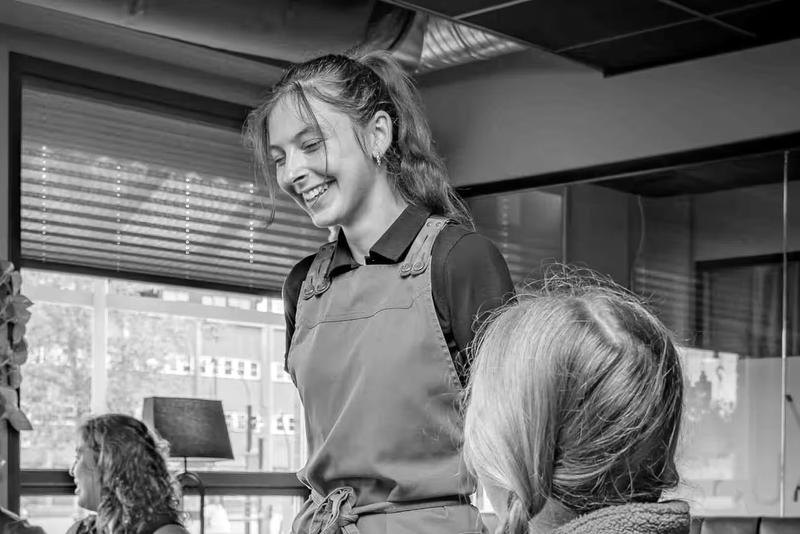 Smilende servitør i forkle ved vinduene i restaurant Raus